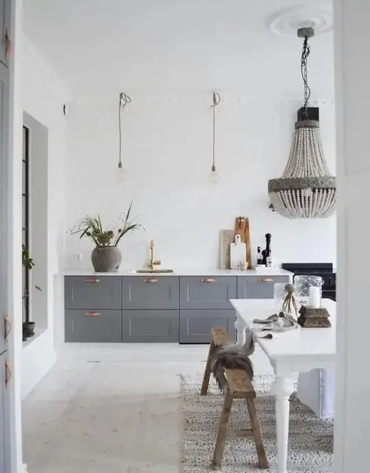A contemporary kitchen with grey cabinets, a white vintage table, pendant lamps, a chandelier, and benches. Combine vintage furniture with modern lighting for a stylish blend of old and new.