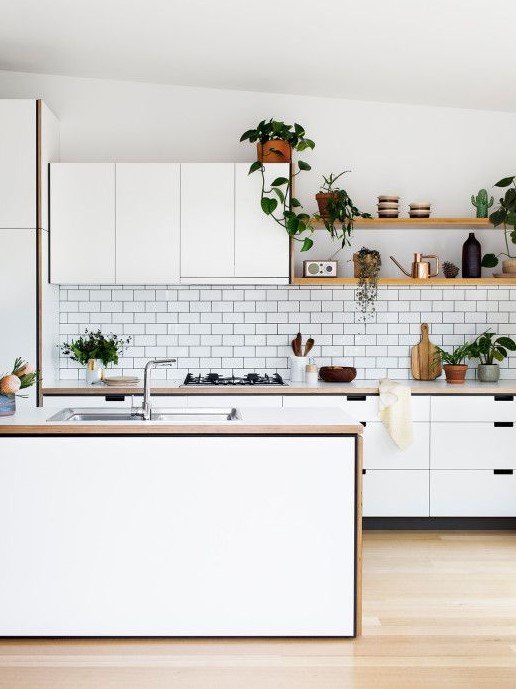 a contemporary white Nordic kitchen with sleek cabinets, wooden countertops, potted greenery and sa white subway tile backsplash