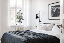 a contrasting Scandinavian bedroom with a black bed and black and white bedding, an artwork, black sconces and potted greenery
