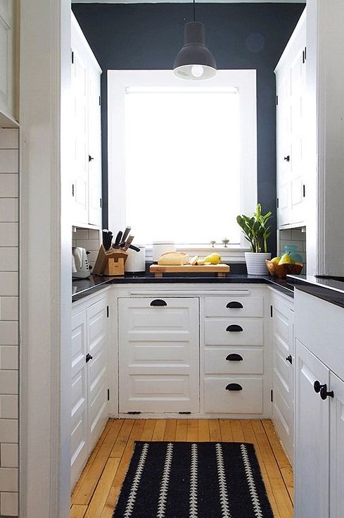 a contrasting U shaped kitchen with white cabinetry, navy walls, black fixtures and black countertops is super chic
