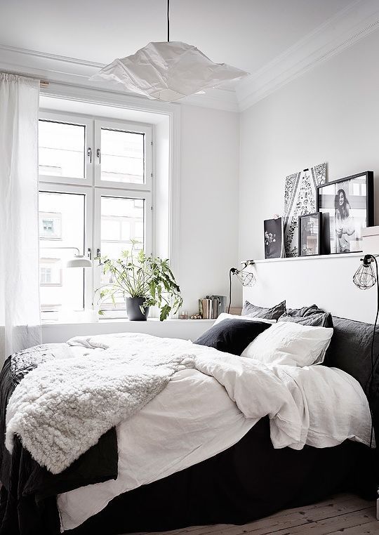 a contrasting bedroom with a black bed with black and white bedding, a ledge gallery wall and a pendant lamp