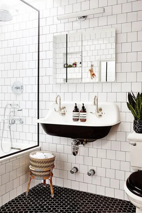 a contrasting modern bathroom with white square tiles and hex tiles on the floor, a black wall mounted sink, a mirror and some potted plants