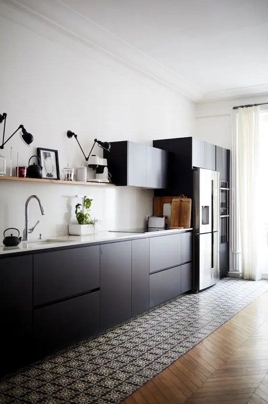 A cool Scandinavian kitchen with matte black cabinets, white countertops and a backsplash, an open shelf and black and white tiles on the floor.