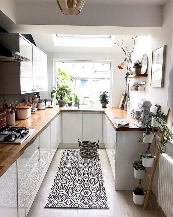 a cool contemporary U-shaped kitchen with sleek white cabinets, butcherblock countertops, a bold rug and potted plants
