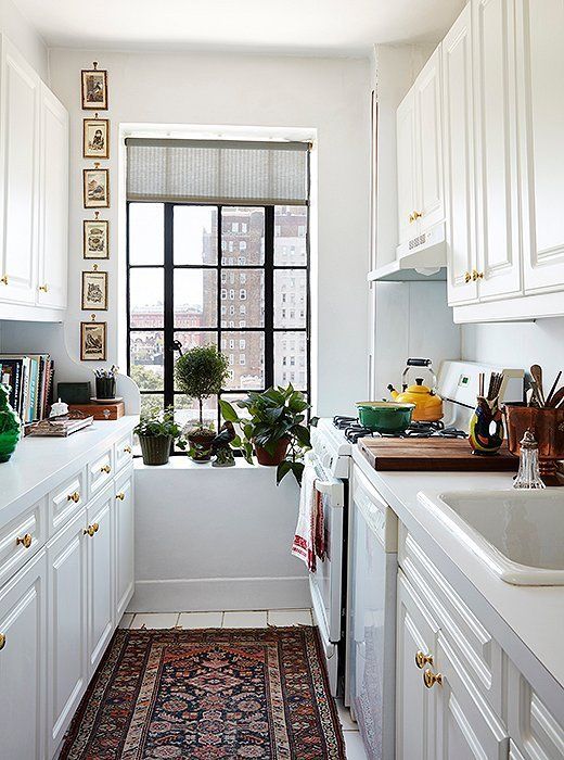 a cool galley kitchen with white cabinets, a boho rug, potted greenery, a gallery wall and some bright touches