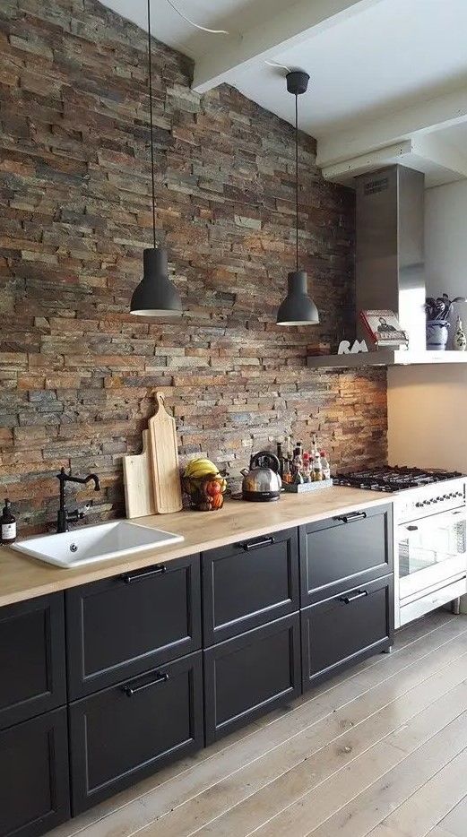 a cozy black one wall kitchen with butcherblock countertops and a faux stone wall plus pendant lamps is chic