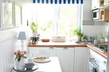 a cozy coastal kitchen with white cabinetry, bold countertops, striped and plaid textiles and a pendant lamps