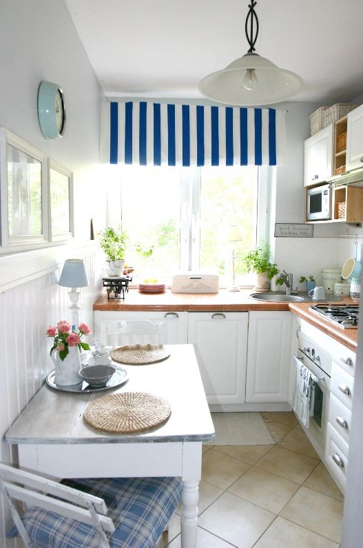 a cozy coastal kitchen with white cabinetry, bold countertops, striped and plaid textiles and a pendant lamps