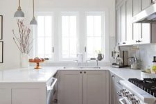 a cozy grey U-shaped kitchen with white stone countertops, a white marble tile backsplash and elegant lamps