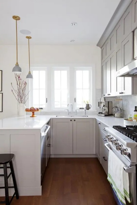 a cozy grey U-shaped kitchen with white stone countertops, a white marble tile backsplash and elegant lamps