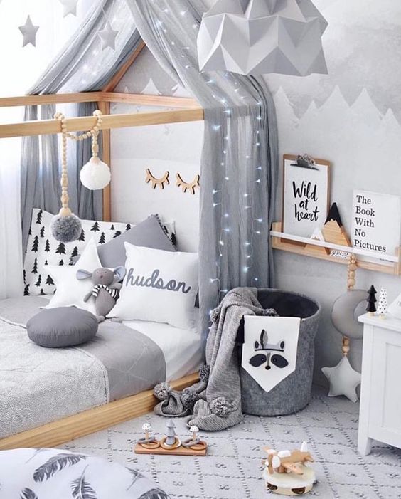a dreamy Scandinavian bedroom with a house shaped bed, a ledge for art, a felt basket with blankets and some ligts and stars