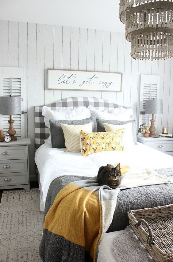 a farmhouse bedroom in light greys, a plaid upholstered bed, grey furniture, a beaded chandelier and grey and yellow bedding