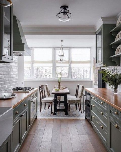 a galley kitchen with green cabinetry, butcherblock countertops, a large window, a dining table and chairs and pendant lamps