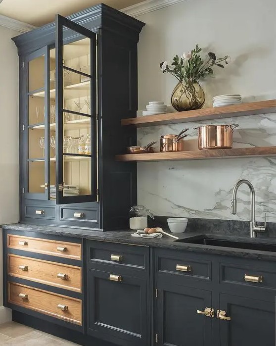 A graphite grey vintage kitchen with gold handles, a black stone countertop and a white stone backsplash.
