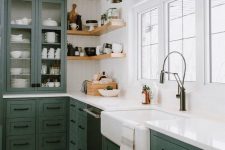 a green farmhouse L-shaped kitchen with shaker cabinets, corner shelves, black sconces, white countertops and a backsplash