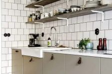 a greige Scandinavian kitchen with leather pulls, a white square tile wall and open shelves and grey sconces