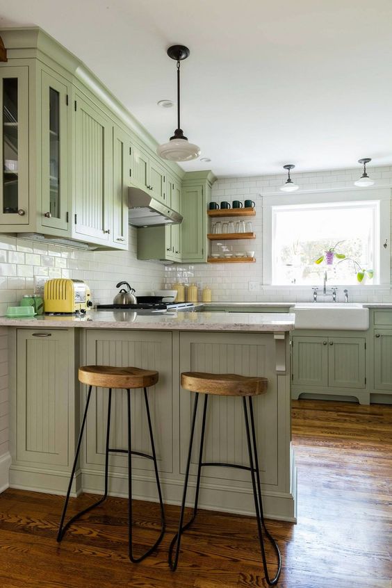 a green farmhouse U-shaped kitchen with planked cabinets, stone countertops, pendant lamps and wooden stools