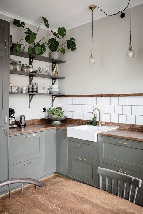 A grey L shaped Scandinavian kitchen with a white square tile backsplash, open shelves, pendant lamps and a stained table