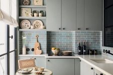a grey L-shaped kitchen with sleek cabinets, white stone countertops, a blue and grey subway tile backsplash, a tiny table and chairs