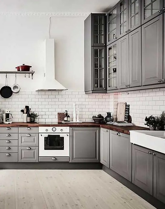 A grey Scandinavian kitchen with rich stained butcherblock countertops and a white tile backsplash plus white appliances