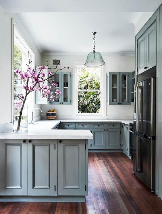 a grey U-shaped kitchen with shaker cabinets, white stone countertops, windows for natural light and some blooms