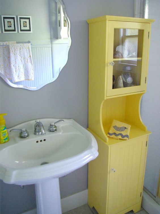 a grey bathroom with a bold yellow cabinet, some white appliances and a wavy edge mirror is a cute space