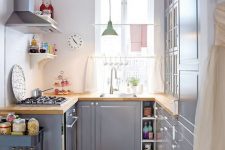 a grey kitchen with butcherblock countertops, a pastel pendant lamp and a grey cart for additional storage