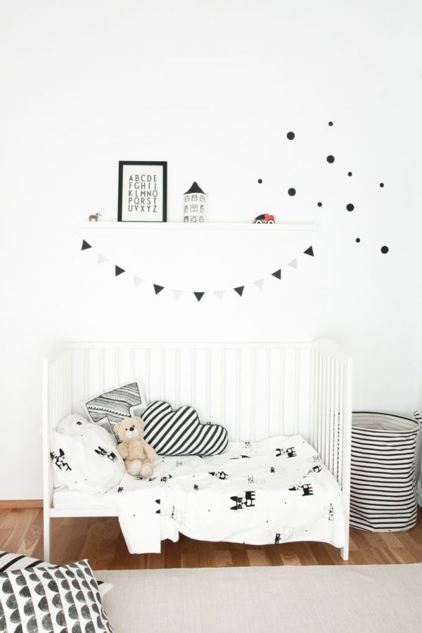 a laconic black and white Scandinavian kid’s room with a white bed, a striped fabric basket, some pillows and a ledge with art