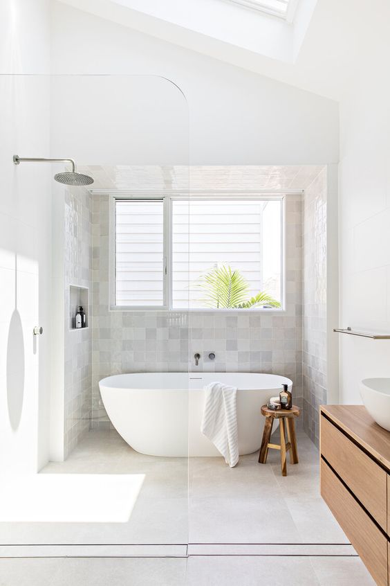 A light filled Scandinavian bathroom clad with neutral tiles, a shower and tub space, a stained vanity, a sink and a skylight