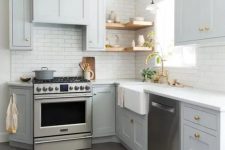 a light grey L-shaped kitchen with open shelves, a white tile backsplash and gold handles is a very stylish and cozy space