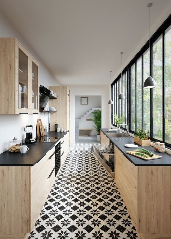a light stained plywood kitchen with black countertops, a glazed wall, black shelves and pendant lamps