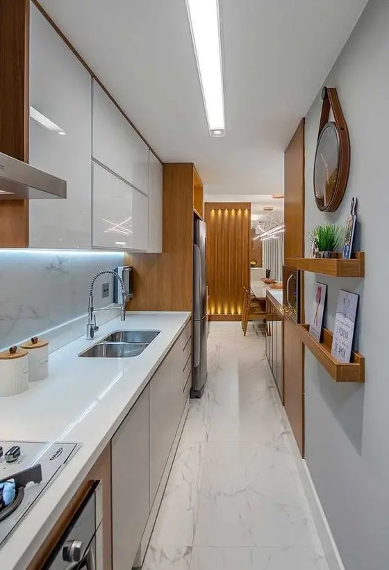 A long narrow kitchen with sleek white and grey cabinets, ledges, built-in lights and some pretty decor.