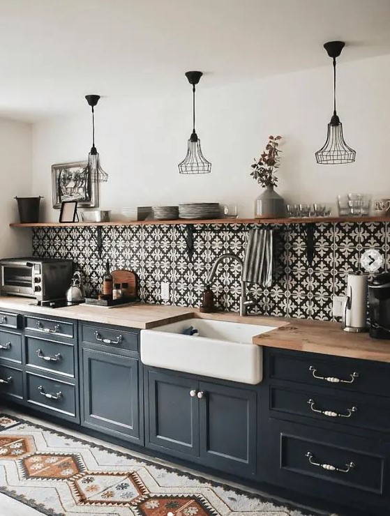A mid-century modern black one wall kitchen with butcherblock countertops, a patterned tile backsplash and metal pendant lamps.