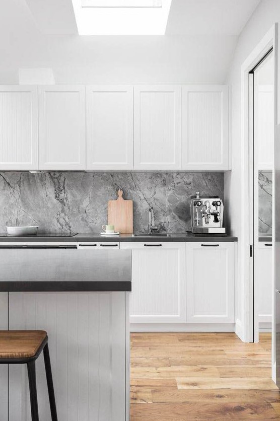 a minimal Nordic kitchen with white paneled cabinets, a grey stone backsplash, black countertops and a wooden floor