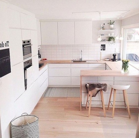 A minimalist Scandinavian kitchen with sleek white cabinets, light staiend countertops, stools and built in appliances