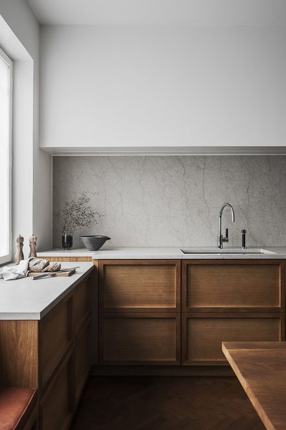 a minimalist Scandinavian kitchen with sleek white uppers, paneled wood lower cabinets, a stone backsplash and countertops