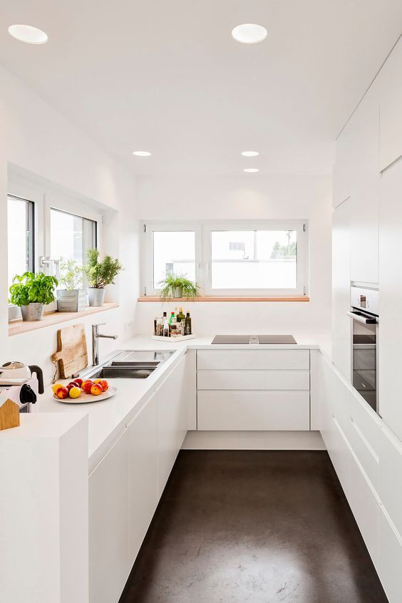 a minimalist U-shaped kitchen with built-in appliances, potted herbs and windows that bring in some light