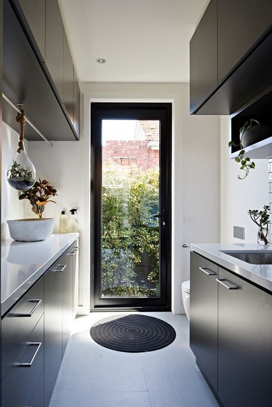 a minimalist black and white kitchen with suspended and usual potted plants, natural light coming through a door