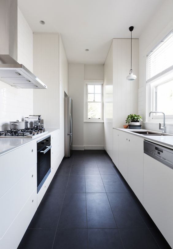 a minimalist gallery kitchen in black and white, with a tiled floor, sleek white kitchens, enough natural light and pendant lamps