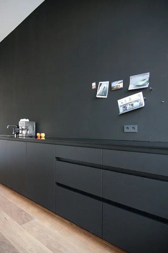 A minimalist matte black kitchen with only lower cabinets, a glossy countertop and a sink, some photos on the wall is a chic and cool space.