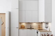 a minimalist white L-shaped kitchen with a brick backsplash, butcherblock countertops and built-in lights