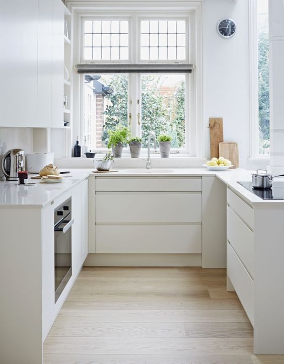 a minimalist white U-shaped kitchen with sleek cabinets, countertops and built-in appliances plus a lot of natural light