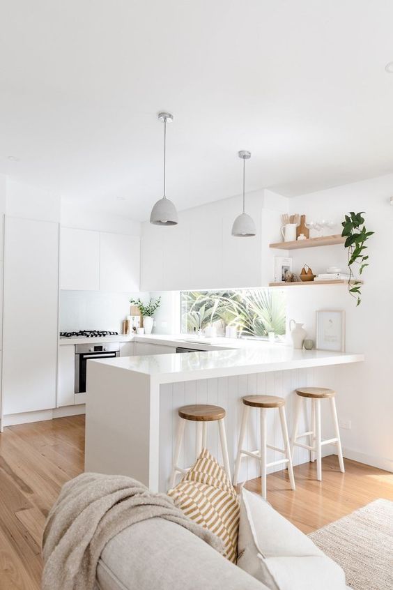 a minimalist white kitchen with sleek cabinets, a window backsplash and wooden stools, pendant lamps