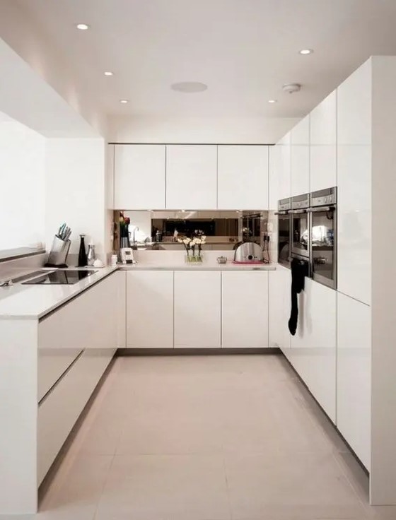 a minimalist white kitchen with white countertops and shiny staineless steel appliances is a very stylish idea