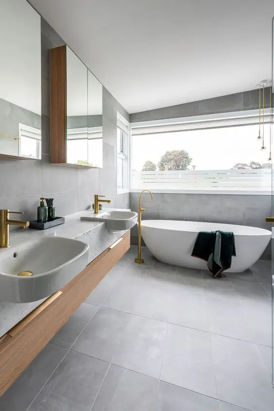 a modern Scandinavian bathroom clad with grey tiles, with a double vanity and mirror cabinets, an oval tub and a window with a view