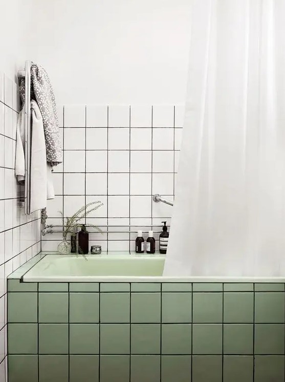 a modern bathroom with square white and green tiles, a light green tub, some neutral textiles and decor