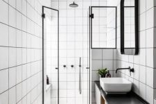 a modern bathroom with white square tiles, a floating black vanity, a shower space, a sink, a mirror in a frame and some lights