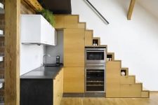 a modern contrasting kitchen with a stained timber staircase that includes cabinets, more cabinets in timber and white and black countertops