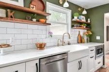 a modern farmhouse kitchen with green walls, white tiles, white cabinets and stone countertops, gold sconces