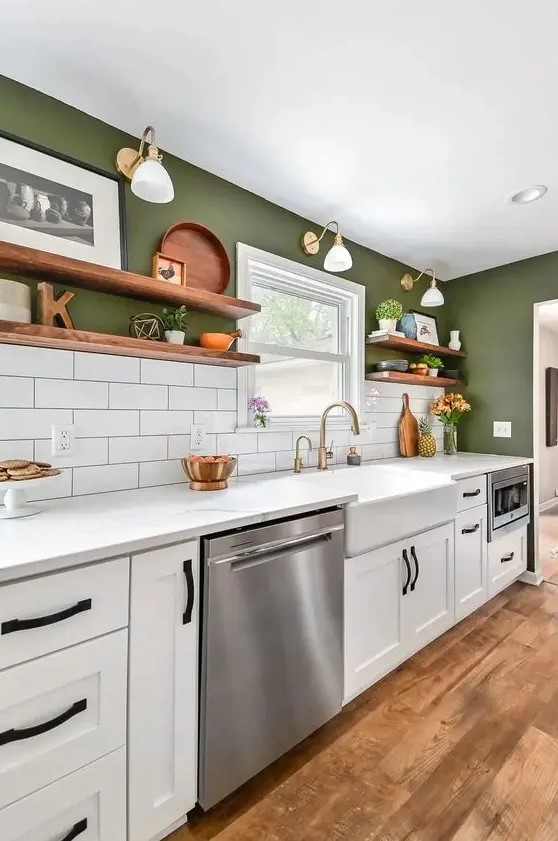 A modern farmhouse kitchen with green walls, white tiles, white cabinets and stone countertops, gold sconces.